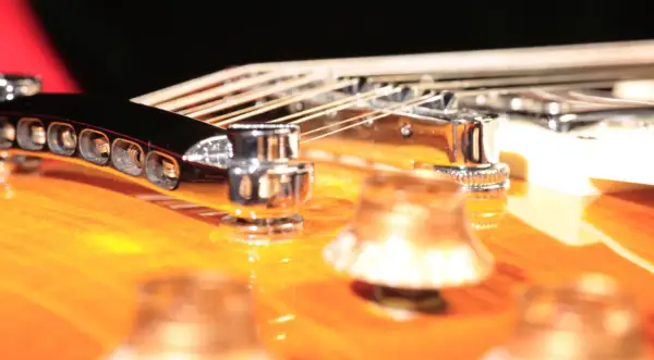 Nahaufnahme einer 12-saitigen Gitarre mit glänzenden Saiten und Chromteilen auf einem orangefarbenen Korpus.
